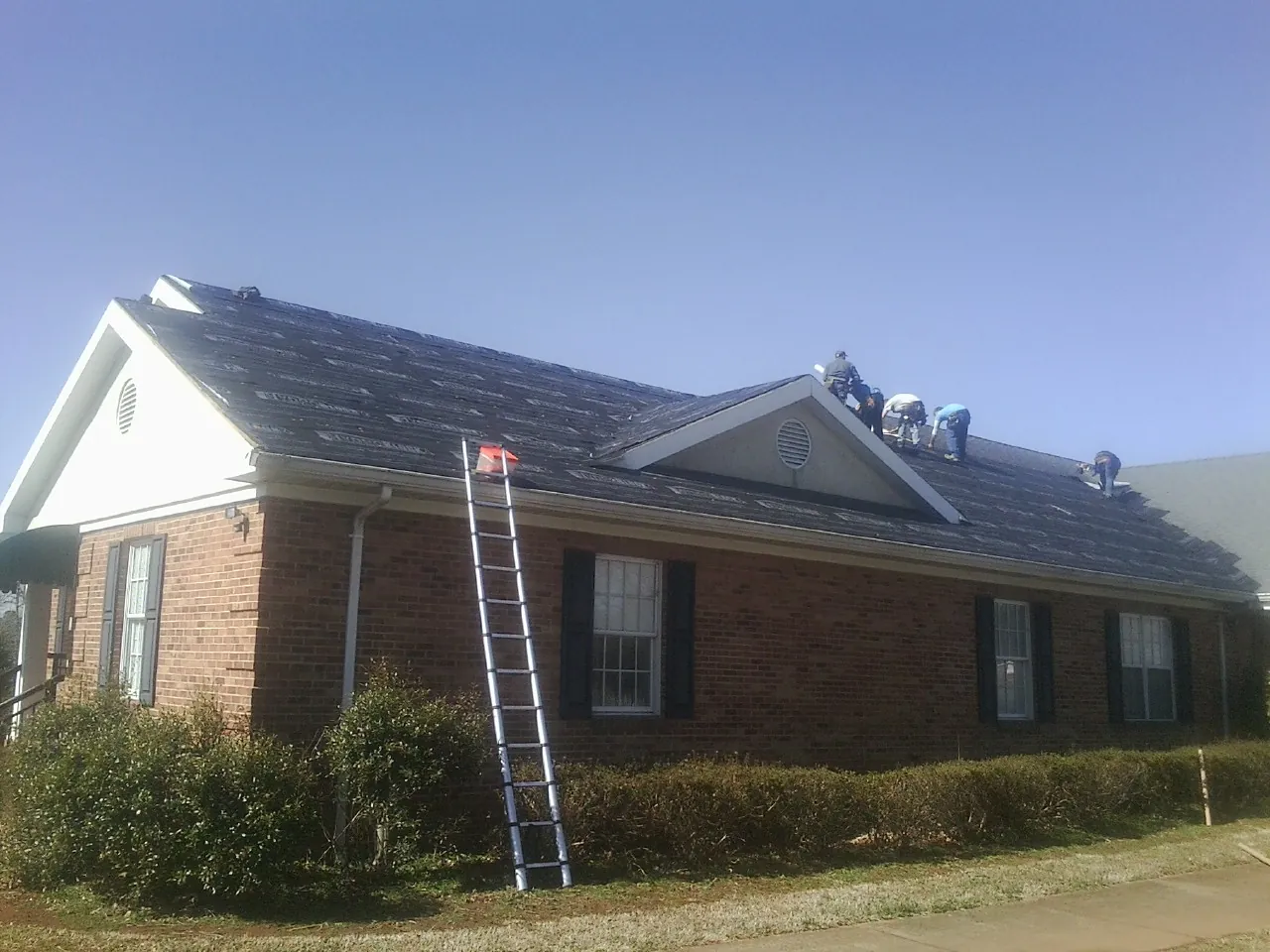 Crew tearing shingles off a brick ranch roof with a ladder set — Metal Roof Repair work by our crew in New Zion