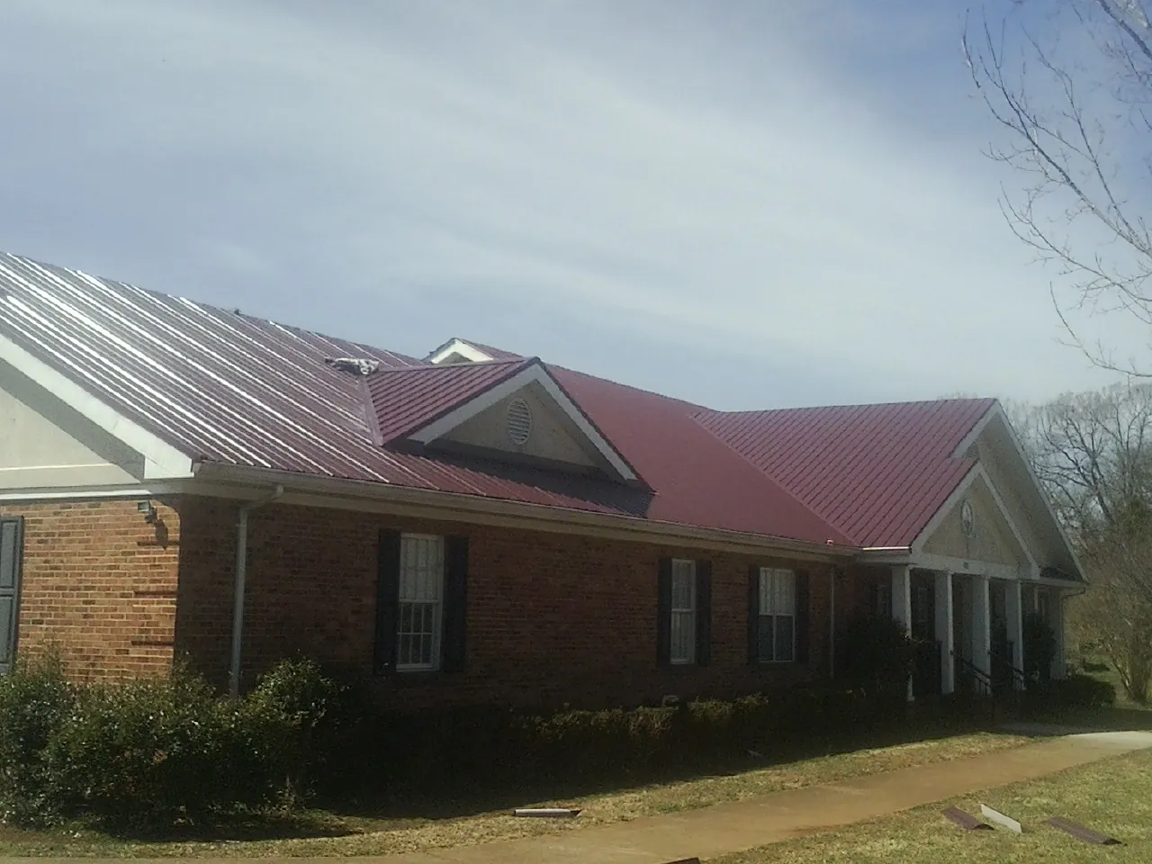 Red metal roof with gabled entries on a long brick building, from a Hail Damage Roof Repair job in New Zion