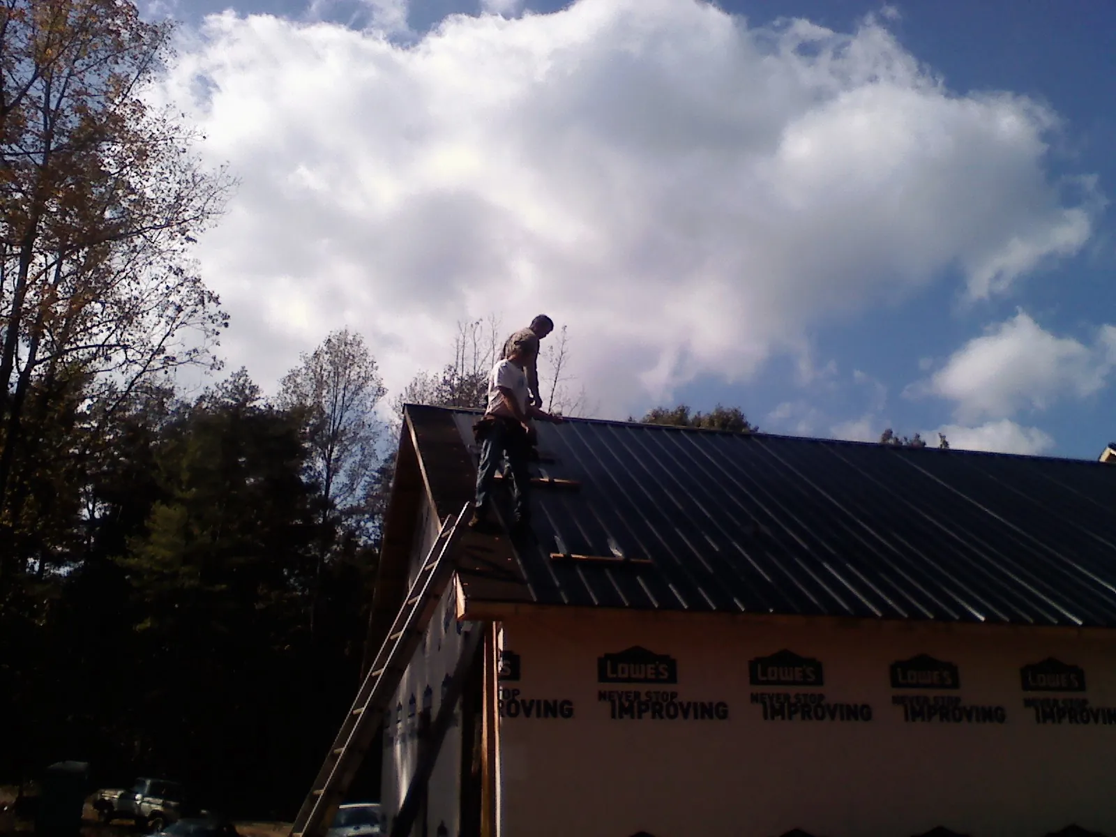 Roofer fastening dark metal panels high against a cloudy sky, from a Roof Inspection job in New Zion