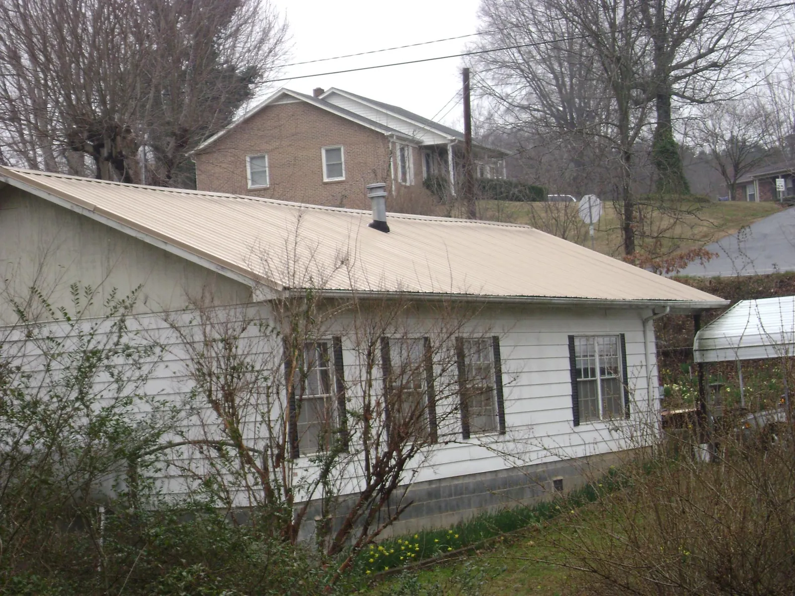 Tan metal roof on a white sided house set into a hillside — Commercial Roofing by Roofing Brothers in New Zion